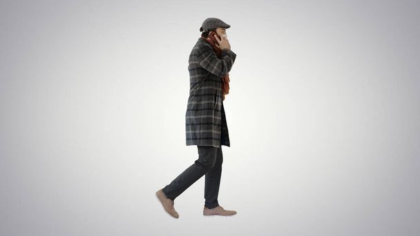 Adult man wears protective medical mask talking on the phone and walking on gradient background. - Foto, afbeelding