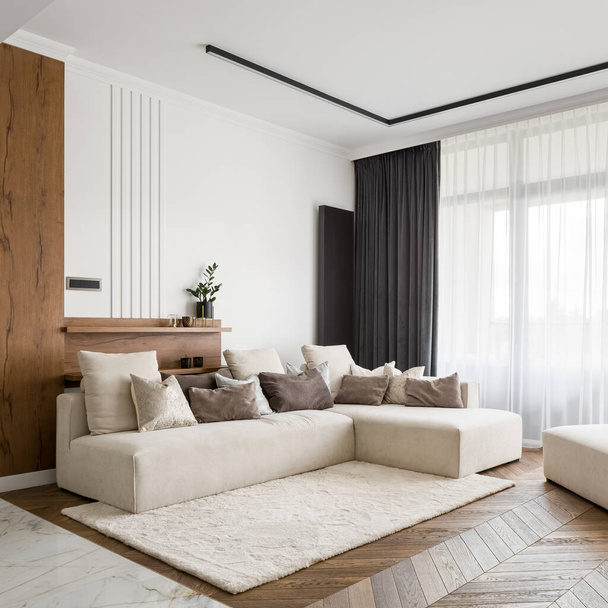Elegantní, světlý a pohodlný obývací pokoj s velkou rohovou pohovkou, dřevěnou podlahou a velkými okny - Fotografie, Obrázek