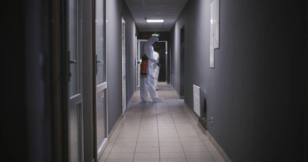 Hombres con trajes de materiales peligrosos desinfectando el edificio
 - Foto, Imagen