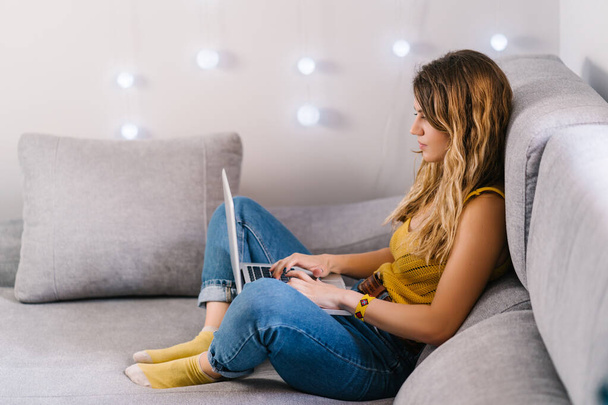 Blonde woman working at home with laptop sitting on sofa at home. - Photo, image