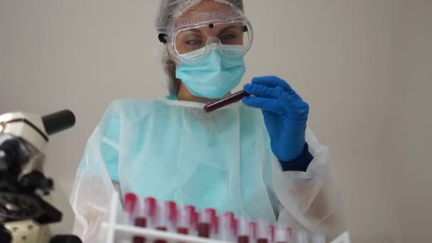 Microbiologist with a tube of biological sample contaminated by Coronavirus with label Covid-19. Lab technician does a chemical blood test. Records the results - Video, Çekim