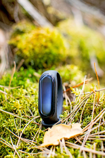Black and blue fitness tracker on forest background. Fitness bracelet for sports training. - 写真・画像
