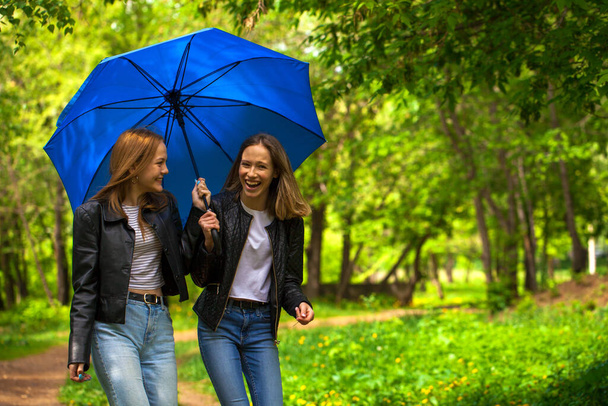 Two cheerful girlfriends walk in the park in rainy weather - Zdjęcie, obraz
