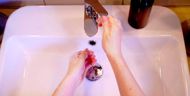 Bovenaanzicht van een vrouw die haar handen wast in een wastafel - Foto, afbeelding
