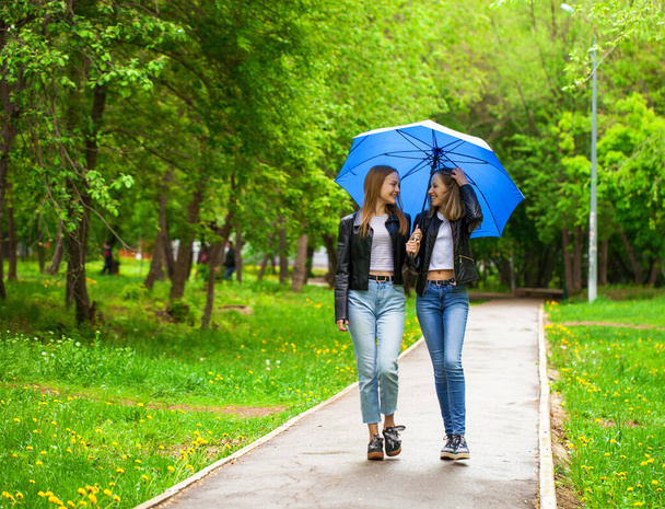 Dwie wesołe dziewczyny spacerują po parku w deszczową pogodę - Zdjęcie, obraz
