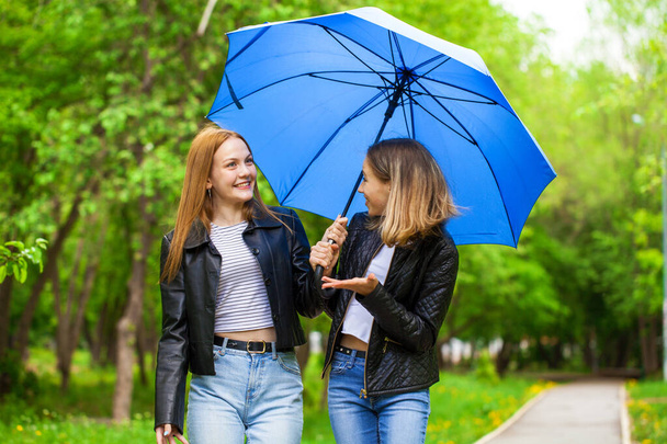 Two cheerful girlfriends walk in the park in rainy weather - Foto, Imagen