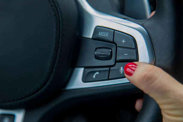 dedo de una mano femenina pulse el botón del micrófono en el volante, el equipo de un coche moderno. primer plano, enfoque suave, fondo borroso
 - Foto, imagen