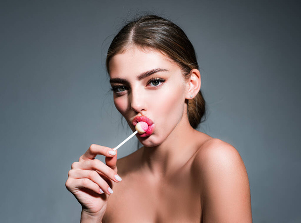 Woman with red lips licking lollipop. Beautiful young woman with clean fresh skin. Sensual woman. High fashion look. Gorgeous female sucks sweets. Beauty fashion portrait. - Foto, Imagen