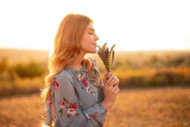 Jovem mulher desfrutando cheiro de flores à noite
 - Foto, Imagem