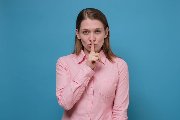 Młoda kobieta trzyma palec na ustach, pokazując cichy gest. - Zdjęcie, obraz