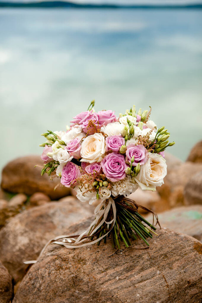 esküvői csokor lila és fehér tónusú rózsa és eustoma, fényképezett köveken a tenger - Fotó, kép