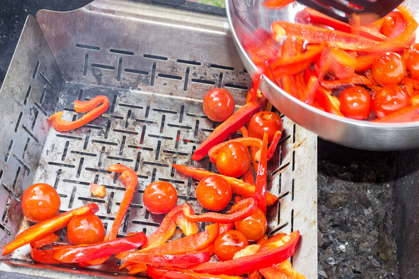 gebakken gesneden groenten-tomaten en rode paprika 's, worden gekookt op een ijzeren grill voor het bakken. De chef gebruikt keukenspatels. Proces van het zelf koken van hete tomatensaus voor pasta of spaghetti - Foto, afbeelding