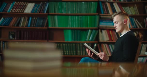 Adam kütüphanede bir sandalyede oturuyor ve yavaşça ilgisini çeken kitabı çeviriyor. 4k - Video, Çekim