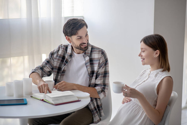 Dark-haired man and his pregnant wife sitting in the kitchen and feeling great - Photo, Image