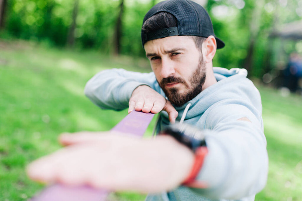 young bearded guy in a blue hoodie pulls slackline for walking - Foto, imagen
