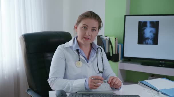 Tıbbi elbise içinde fonendoskop kullanan kadın doktor modern teknoloji kullanarak hastalarla iletişim kuruyor. - Video, Çekim