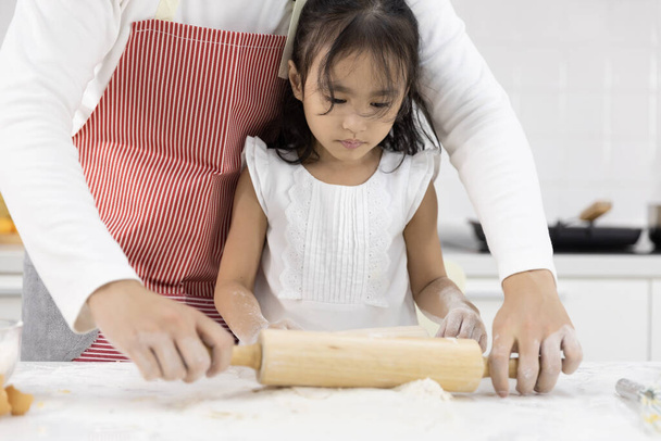 Happy Asian family Father and Daughter are rolling pin thresh flour for making bakery in the kitchen in home. family cooking food Concept. - Фото, изображение
