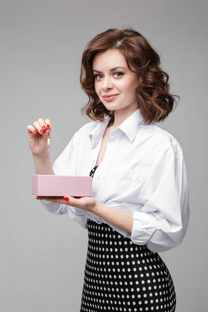 Mulher bonita com corte de cabelo agradável detém um presente com novos brincos, imagem isolada no fundo branco
 - Foto, Imagem