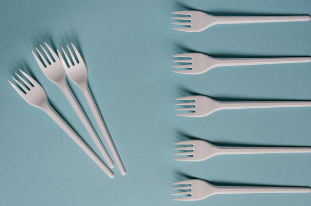 White plastic forks with shadows on a light blue background. Creative background using disposable cutlery. Place for text. View from above. - Photo, Image