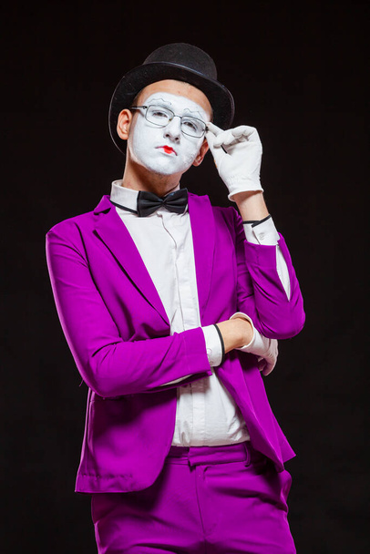 Portrait of male mime artist, isolated on black background. Young man in purple suit is touching his chin with a thoughtful look. Symbol of reflection, criticism - Foto, Imagem