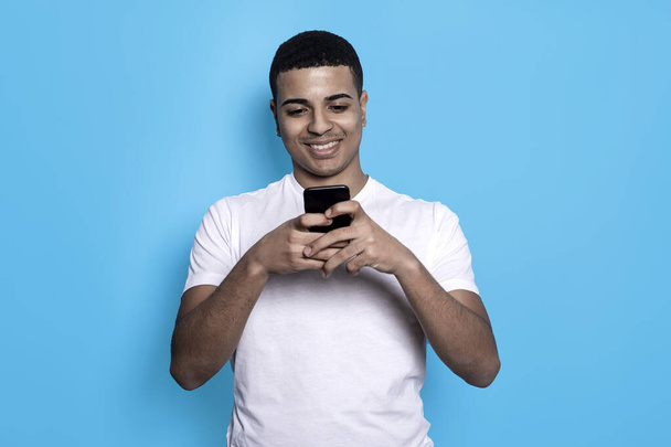 Negro joven macho de pie usando un teléfono móvil sobre un fondo azul
 - Foto, Imagen