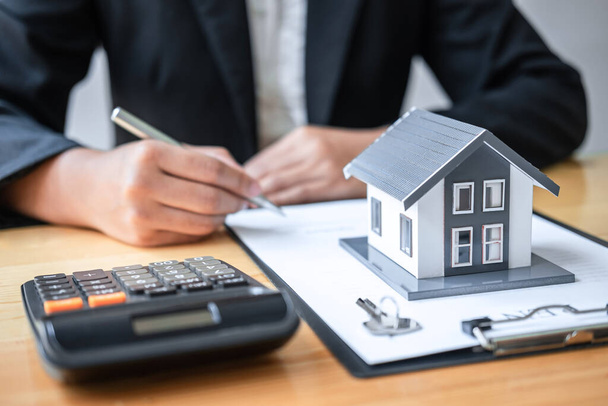 Рабочий агент по недвижимости подписывает договор на страхование дома, одобряющий покупки для клиента с моделью дома и ключом на столе. - Фото, изображение