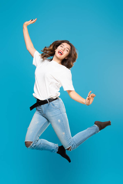 Cute girl student teenager jumping waving hands with a smile on her face on a blue background. The concept of happiness, carefree and positive - Photo, image