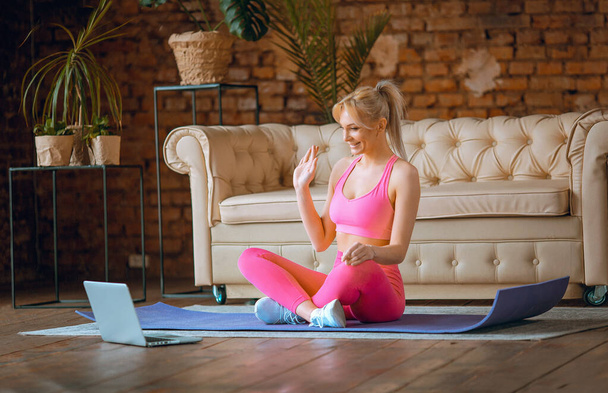 молода дівчина-блогер сидить на килимку для йоги в спортивному вбранні з ноутбуком, що робить онлайн-тренування вдома, записуючи онлайн аеробні навчальні посібники з дому, вправи на камеру
 - Фото, зображення