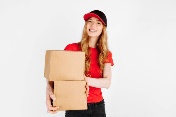 Happy courier girl in uniform holding cardboard boxes on a white background. The concept of home delivery - Фото, изображение