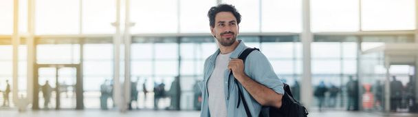 The guy with the backpack at the airport. Young handsome man waiting for boarding, walks through airport terminal - Zdjęcie, obraz