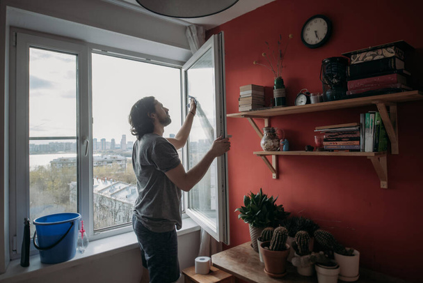 Чоловік миє вікна вдома. Молодий красивий хлопець робить прибирання весни в затишній квартирі
. - Фото, зображення