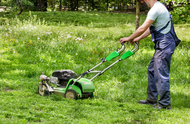 Ein Servicemitarbeiter pflegt den grünen Rasen und mäht das Gras mit einem Benzinmäher. - Foto, Bild