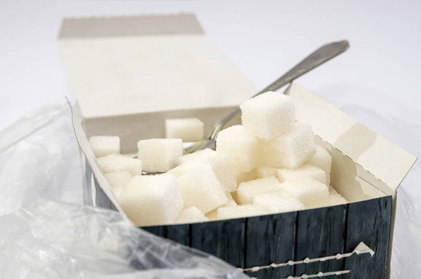 Zuckerwürfel mit einem Löffel in einer Schachtel auf weiß. - Foto, Bild