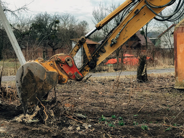 Graafmachine ontwortelt bomen op het land op het platteland. Bulldozer ruimt land op van oude bomen, wortels en takken met vuil en afval. Machines voor graafmachines. Kantoorwerkzaamheden - Foto, afbeelding