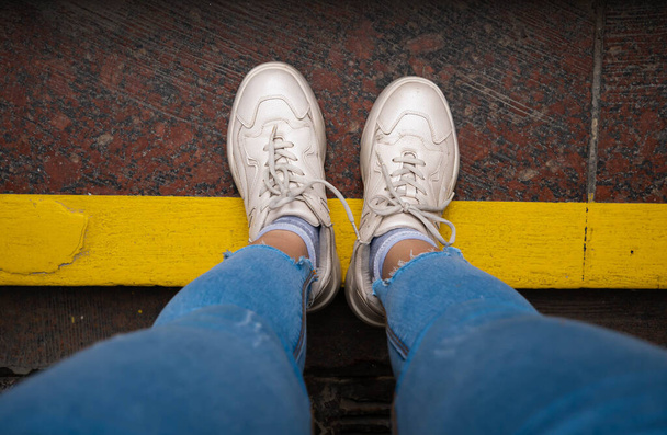 legs in white sneakers Standing Next To Yellow Street Lines. - Фото, изображение