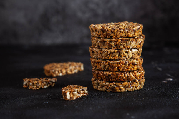 Caramel peanut brittle from sunflower seeds and sesame seeds and fitness cookies with flax seeds on dark black concrete background. - Valokuva, kuva