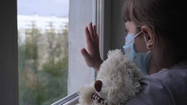 Schattig meisje houdt teddybeer kijken uit venster op straat tijdens quarantaine - Video