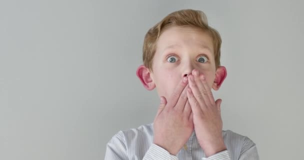 Portret z bliska. Chłopiec jest zaskoczony i zakrywa usta rękami. 4K - Materiał filmowy, wideo