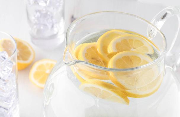 Uma vista de perto de um jarro de água de limão com fatias de limão e dois copos de gelo prontos para derramar
. - Foto, Imagem