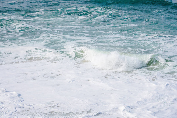 Agua de mar turquesa con pequeñas olas de espuma blanca que chocan suavemente contra la playa de arena dorada
 - Foto, imagen
