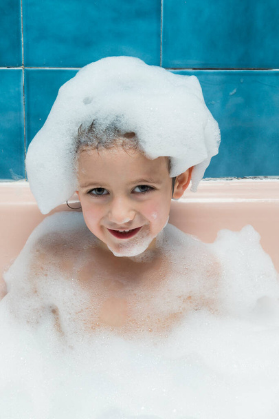 Portrait of a boy in a bathtub with foam, with foam on his head. - Фото, изображение