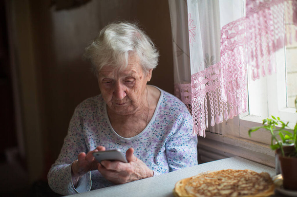 Starší žena sedí s chytrým telefonem v ruce. - Fotografie, Obrázek