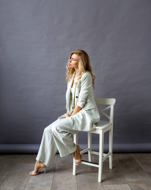 Beautiful blonde woman in a suit sitting on a chair in the studio. - 写真・画像