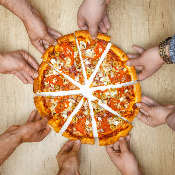 Big delicious pizza is nice dish for dinner or lunch. Closeup picture of pizza represented on wooden table. Many hands are taking it. - Foto, Imagem