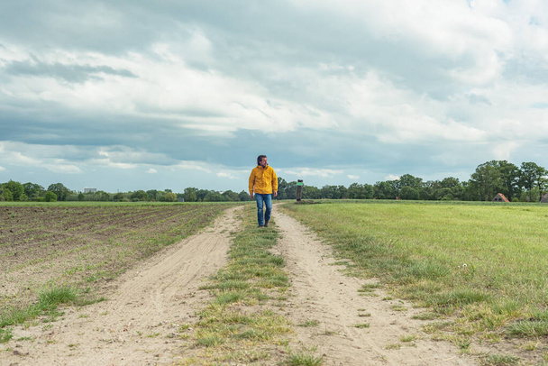 Man in yellow jacket and jeans walks on pathway in meadow. - Фото, зображення