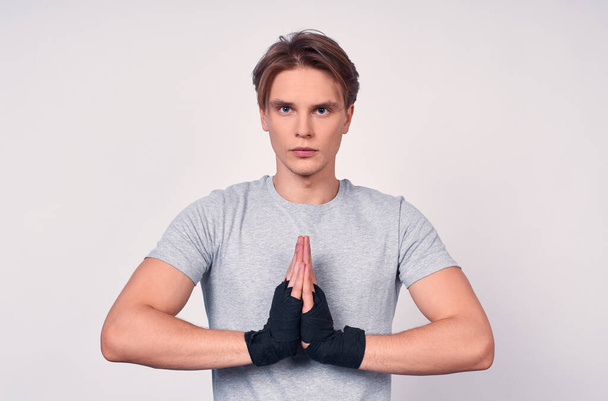 Young pacified altetic nice guy boxer with a black bandage on his hands, in a gray T-shirt, meditates before the fight, looks directly, thinks about victory. - Foto, Bild