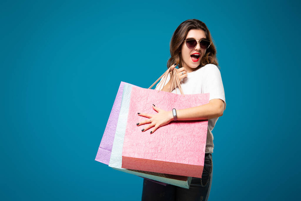 Young stylish beautiful girl in sunglasses is walking with multi-colored shopping bags. Concept shopping and store. - Foto, Imagen