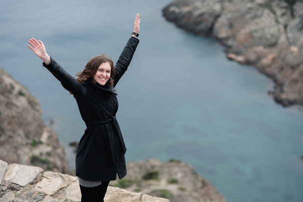 女性は海の前の崖の上の自由の印として腕を空に上げ - 写真・画像