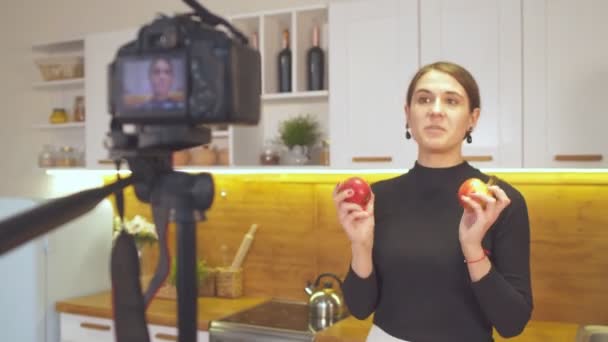 Glückliches junges Mädchen hält Äpfel in der Hand und nimmt ihre Blog-Episode über gesunde Ernährung auf, während sie zu Hause in der Küche steht - Filmmaterial, Video
