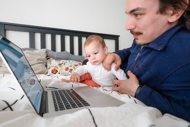 Мужчина пытается работать дома через ноутбук во время карантина с младенцем. Семейная жизнь во время самоизоляции. Сиди дома. Работа из дома, домашний офис
 - Фото, изображение